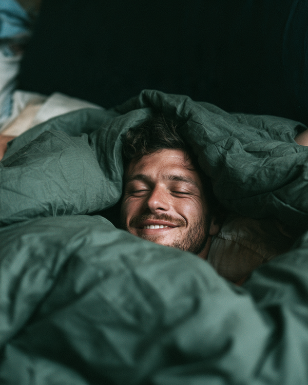 Man smiling while tucked into a cozy green duvet