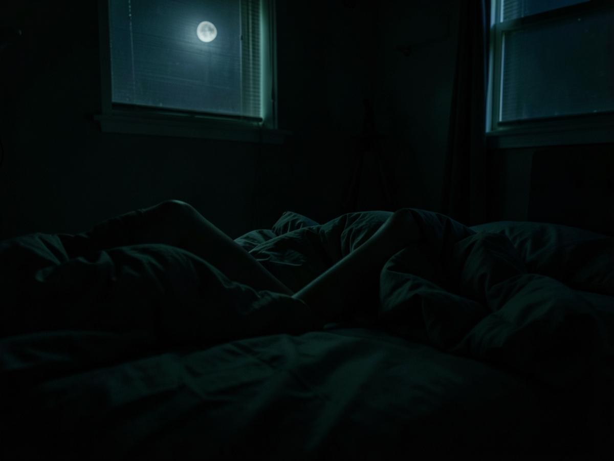 Legs shifting under a duvet in a dark bedroom lit only by moonlight through a window